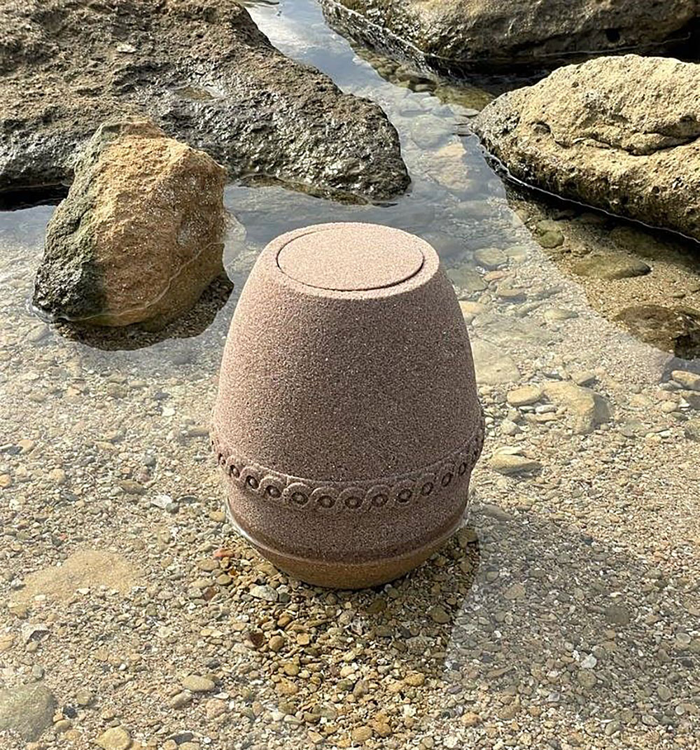 urne-sand-hoy-i-vann-paa-strand Sandurne som står i vannet på en strand.